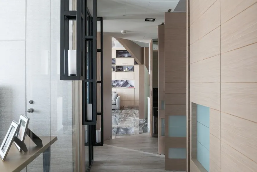 A modern home lobby featuring glass walls, wooden panels, and marble flooring.