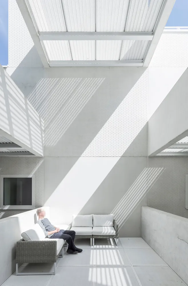 A minimalist interior space with concrete walls and a concrete floor, featuring white furniture and a television.