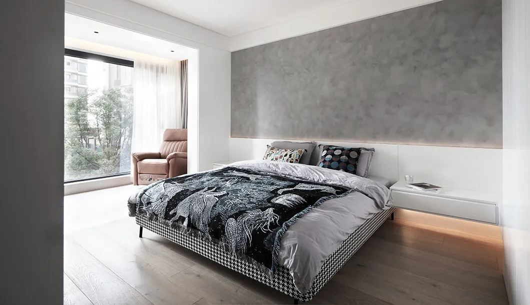 A modern minimalist bedroom featuring a concrete accent wall and a bed with a black and white checkered quilt, set against a 