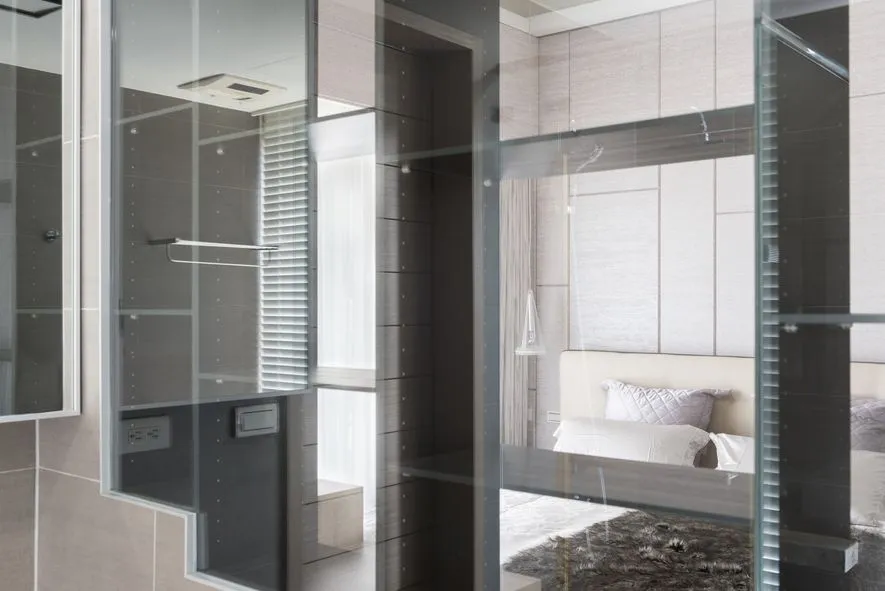 Modern minimalist bedroom featuring glass walls and a white bed.