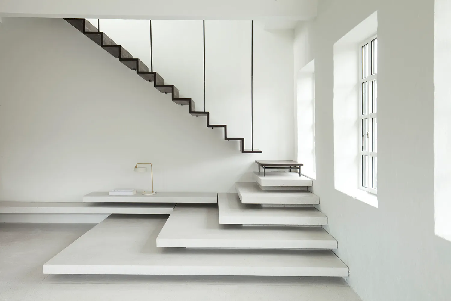 Modern minimalist interior design featuring a concrete staircase with floating steps and a simple, elegant lamp.