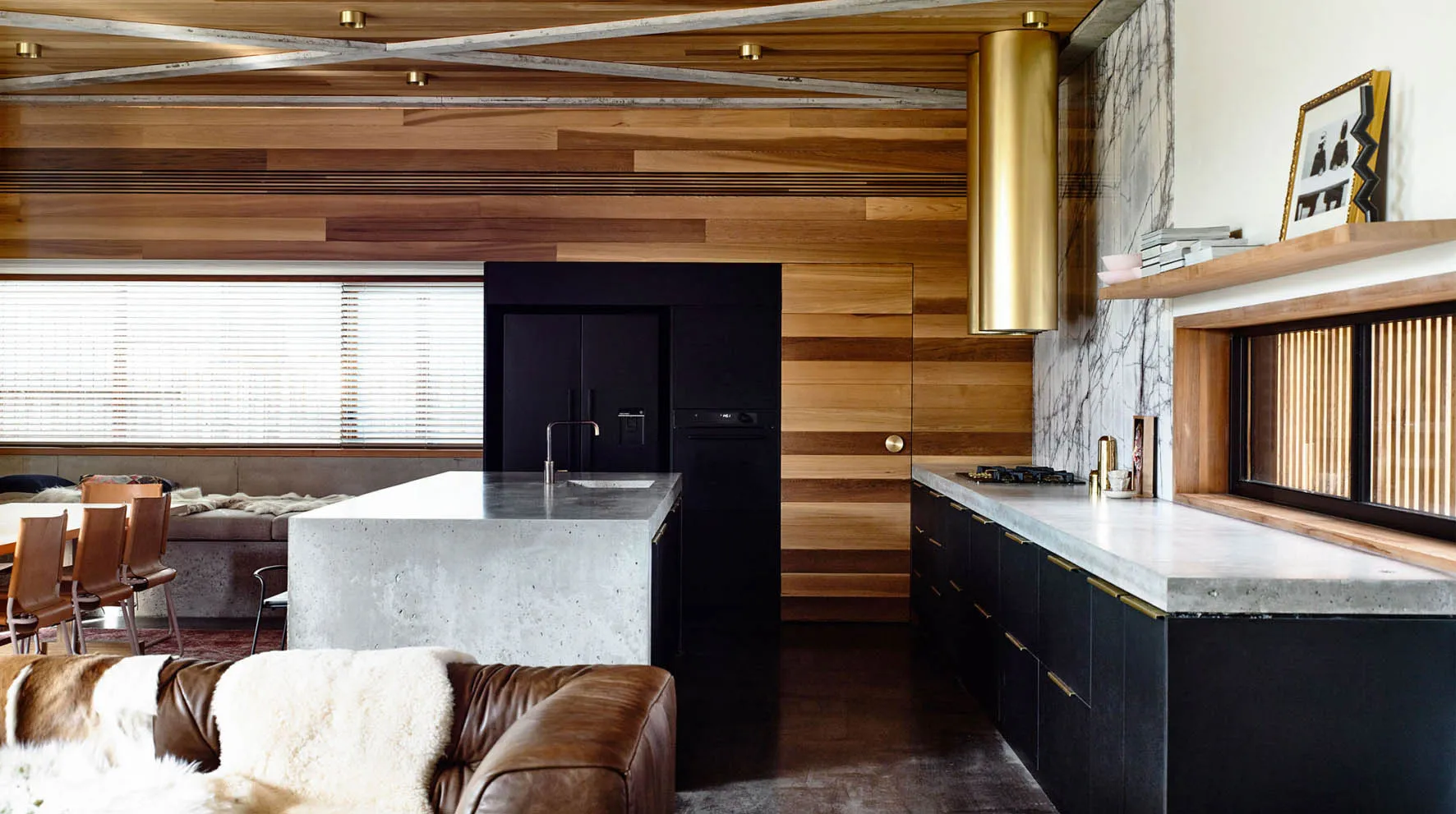 Modern kitchen and dining area featuring concrete countertops, wooden walls, marble flooring, and metal accents.