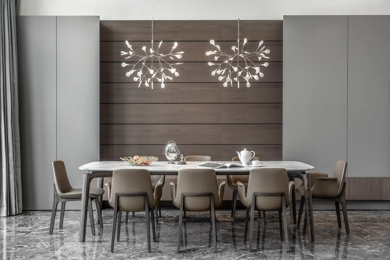 Modern dining room with marble table and chairs, featuring hanging chandeliers and grey cabinetry.