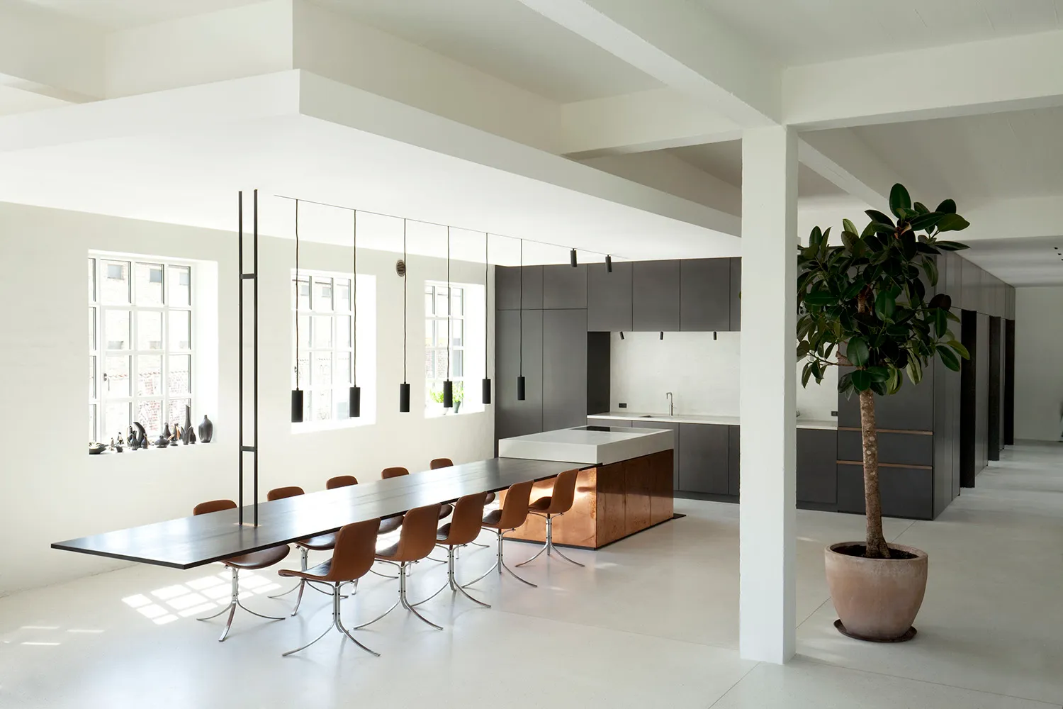 A modern minimalist kitchen with a concrete floor, long dining table, and dark cabinets.