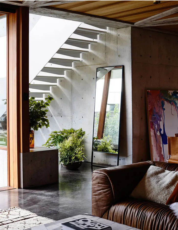 Modern minimalist living room featuring a concrete staircase and a brown leather sofa.