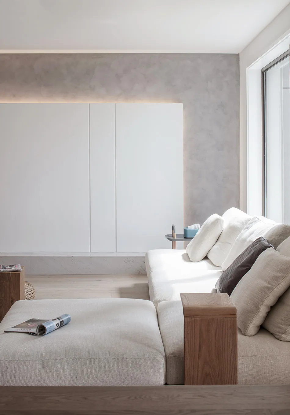 A minimalist living room with a white sofa, neutral-toned cushions, and a wooden ottoman in a neutral-toned space.