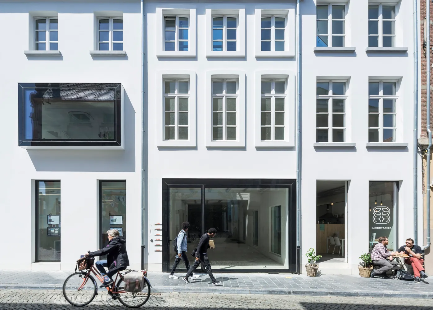 現代街景咖啡店，玻璃與混凝土立面，人們路過，單車騎士經過。