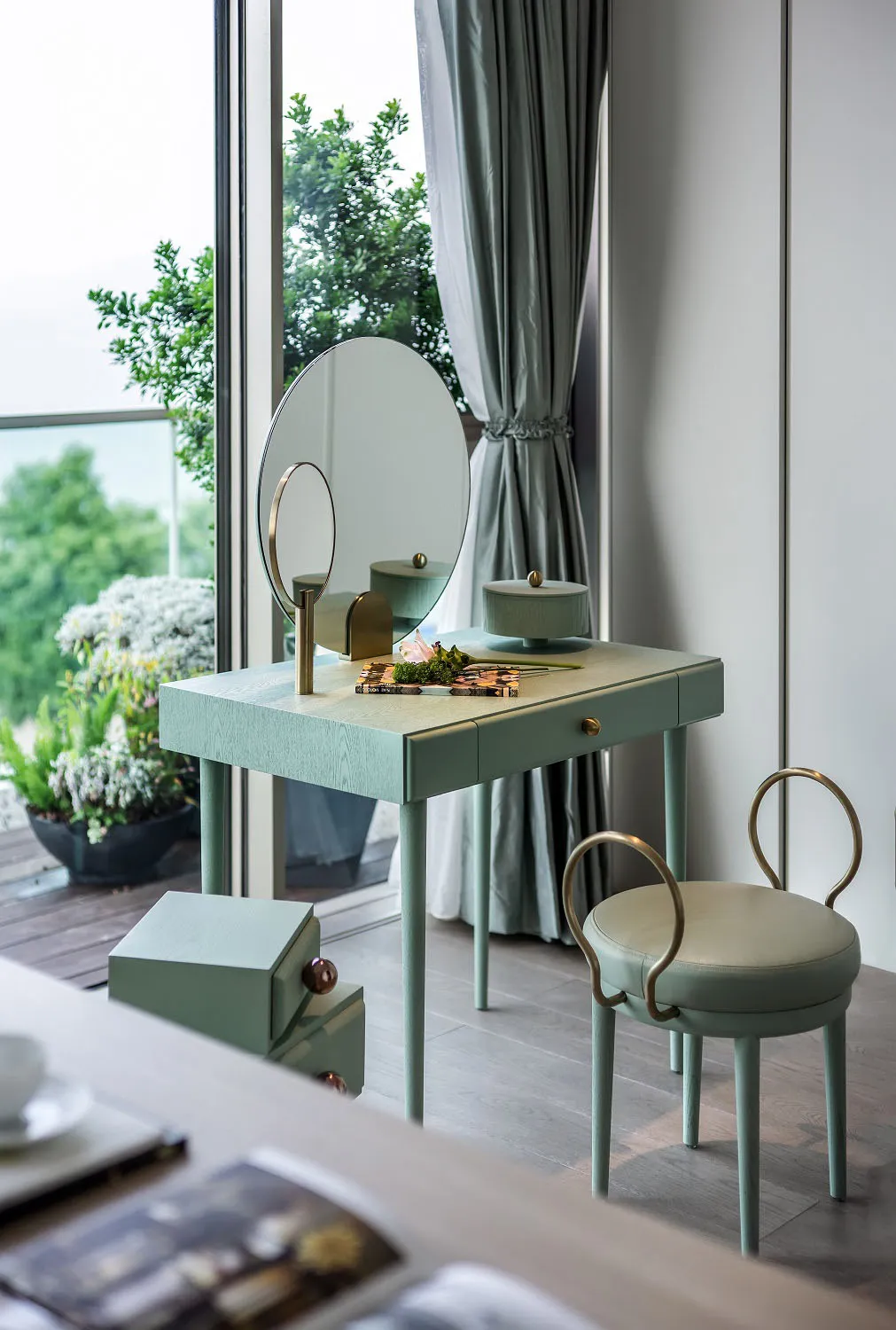 A modern vanity with wooden legs, a circular mirror, and a green cushioned stool.
