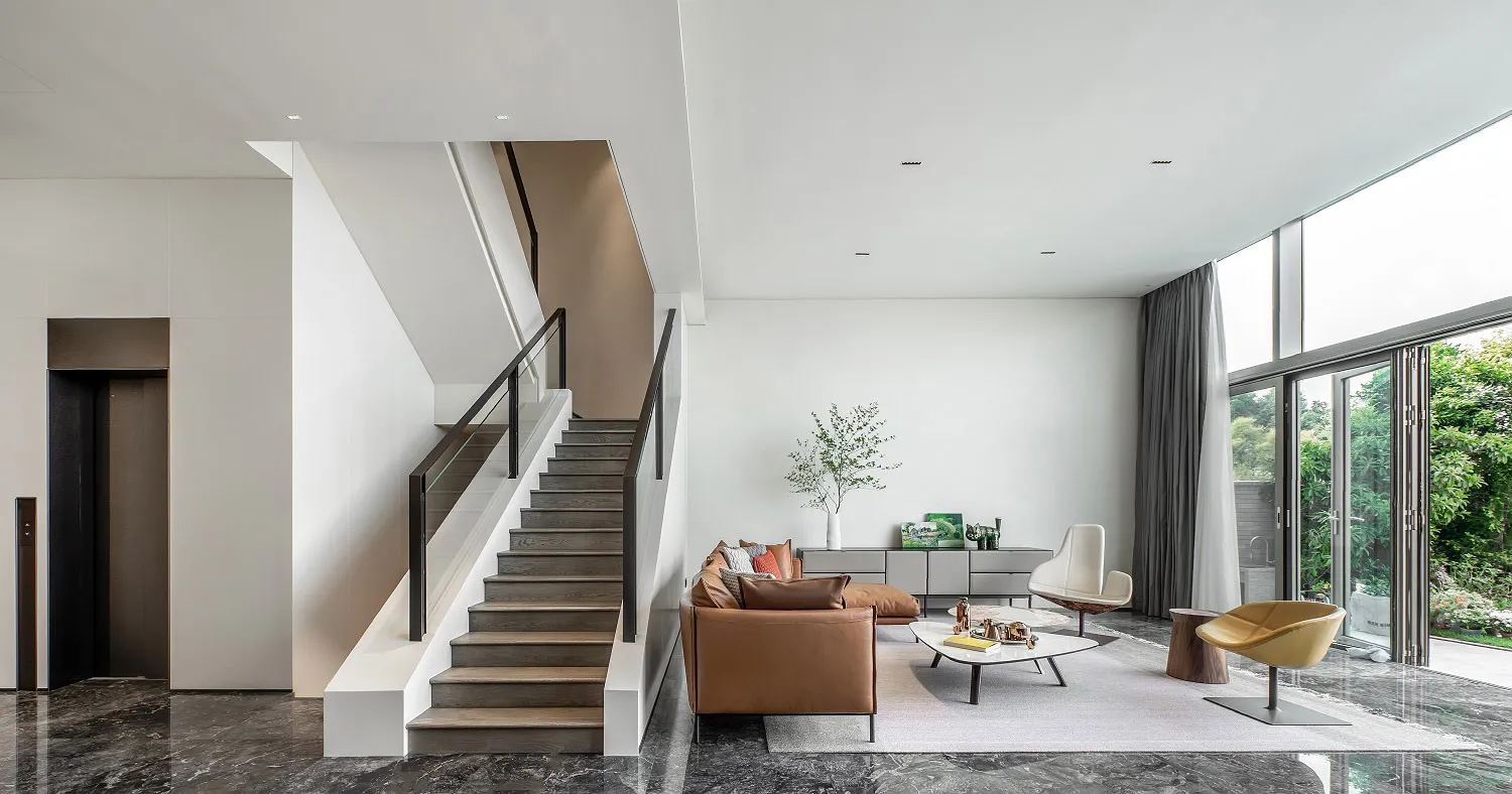 A modern minimalist living room with a brown leather sofa, white coffee table, and large windows.