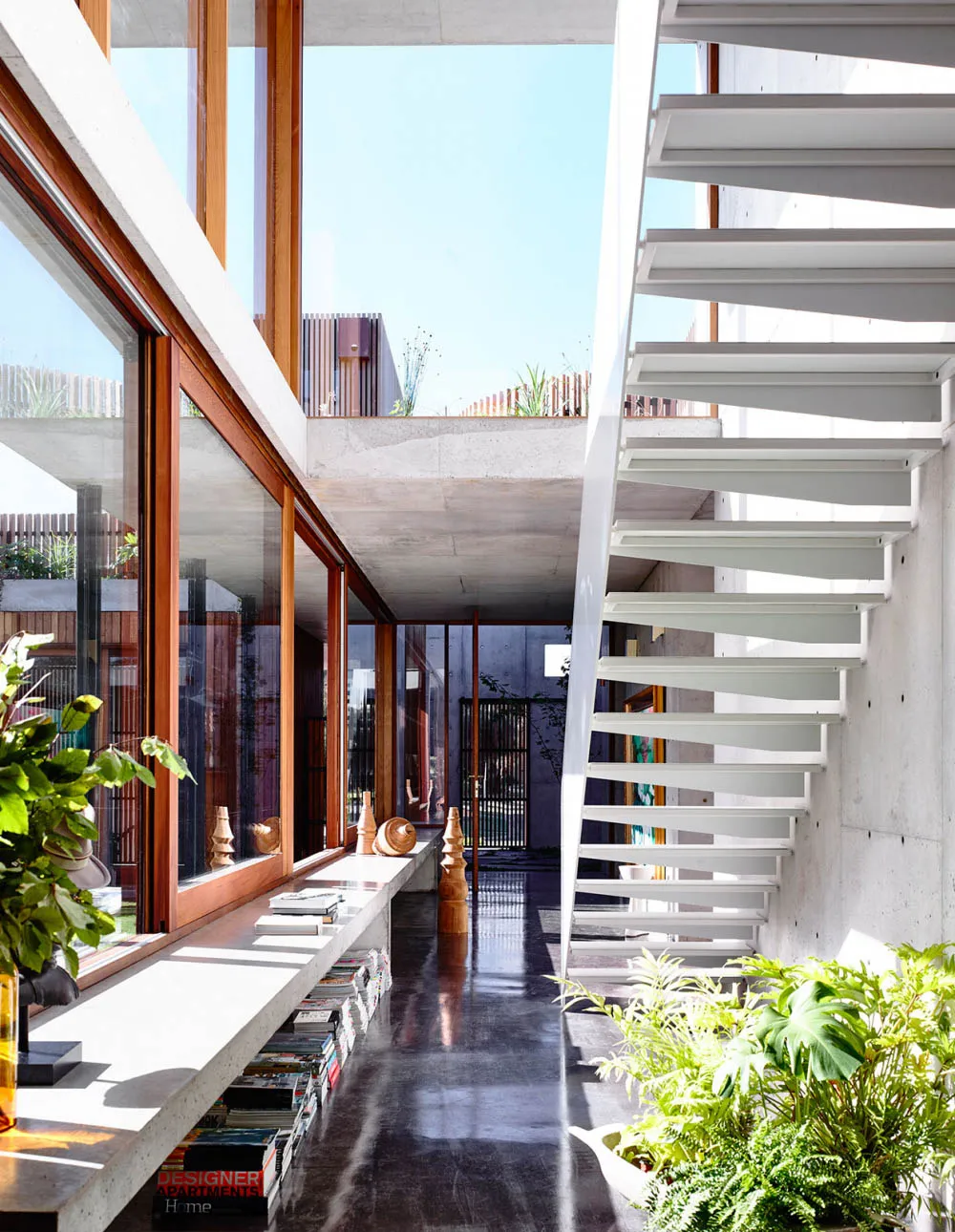 A modern, minimalist staircase with white steps, surrounded by indoor plants and a floor-to-ceiling window.
