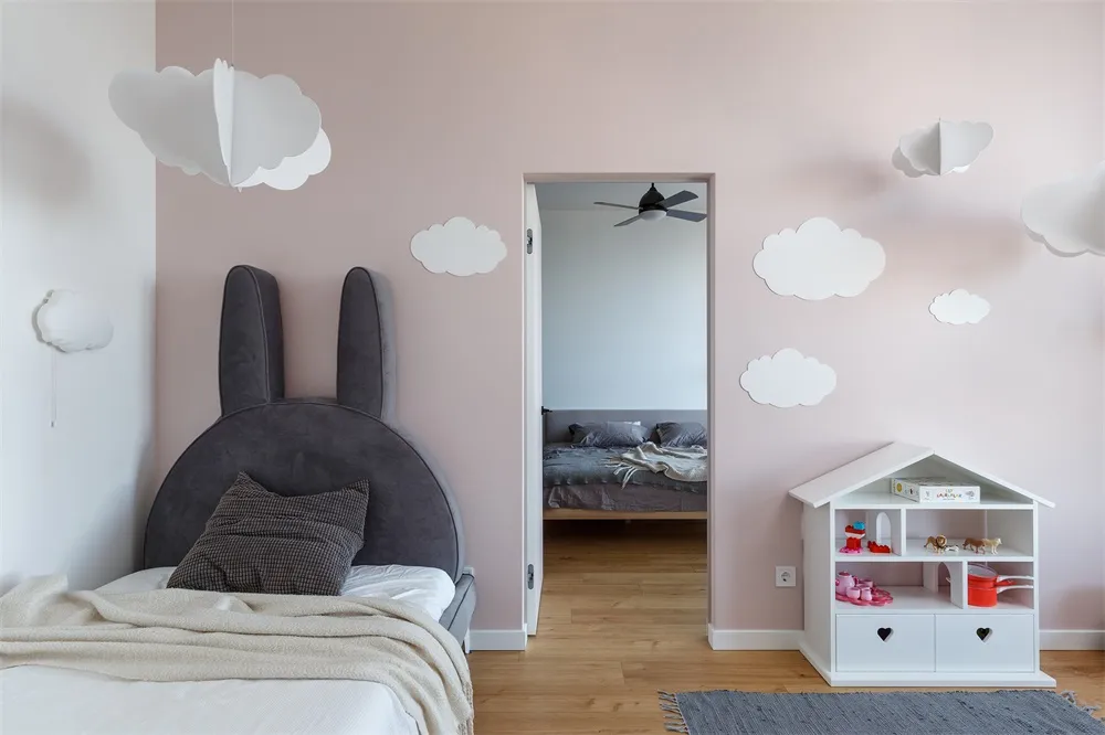 Children's bedroom featuring pink walls with white paper clouds, a bed with a bunny-shaped headboard, and a small white dollh