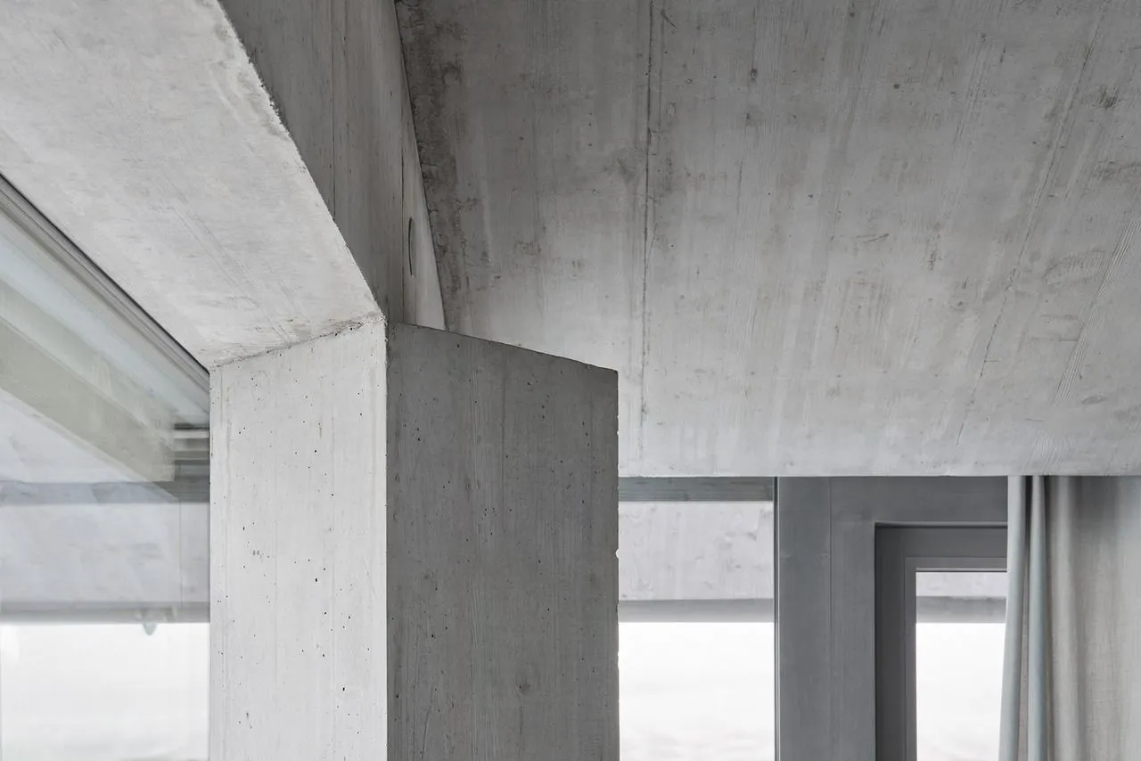 A minimalist concrete living room with exposed concrete surfaces, large windows, and simple furniture.