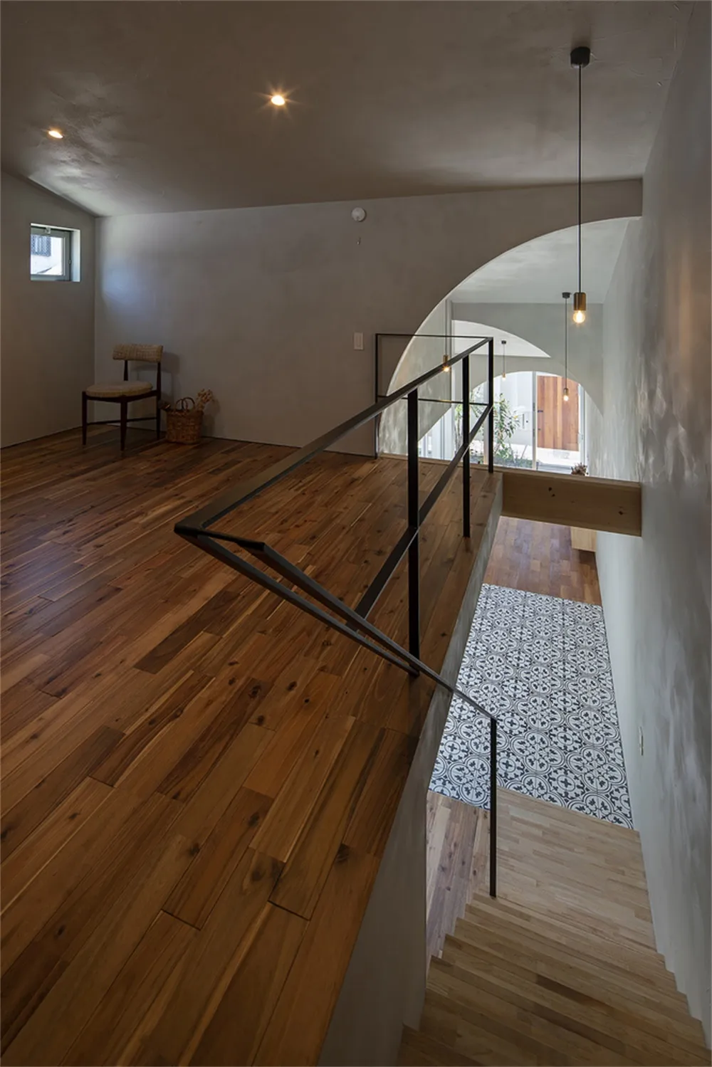A modern house interior with a wooden staircase, glass railing, and patterned floor tiles.