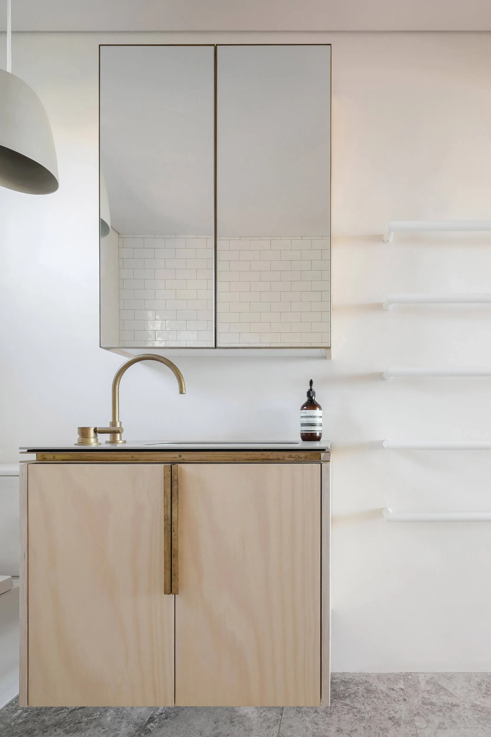 A modern minimalist bathroom featuring a wooden cabinet with a brass faucet and a white tiled wall.