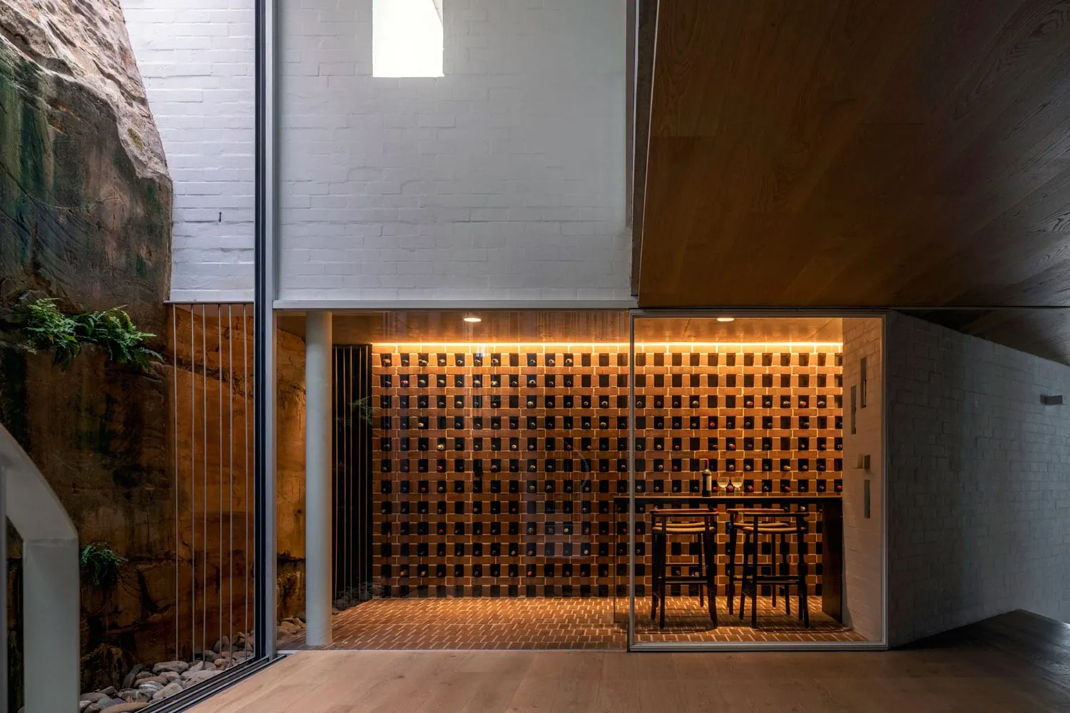A minimalist wine cellar lined with brick, illuminated by warm lighting, featuring a bar counter and chairs.