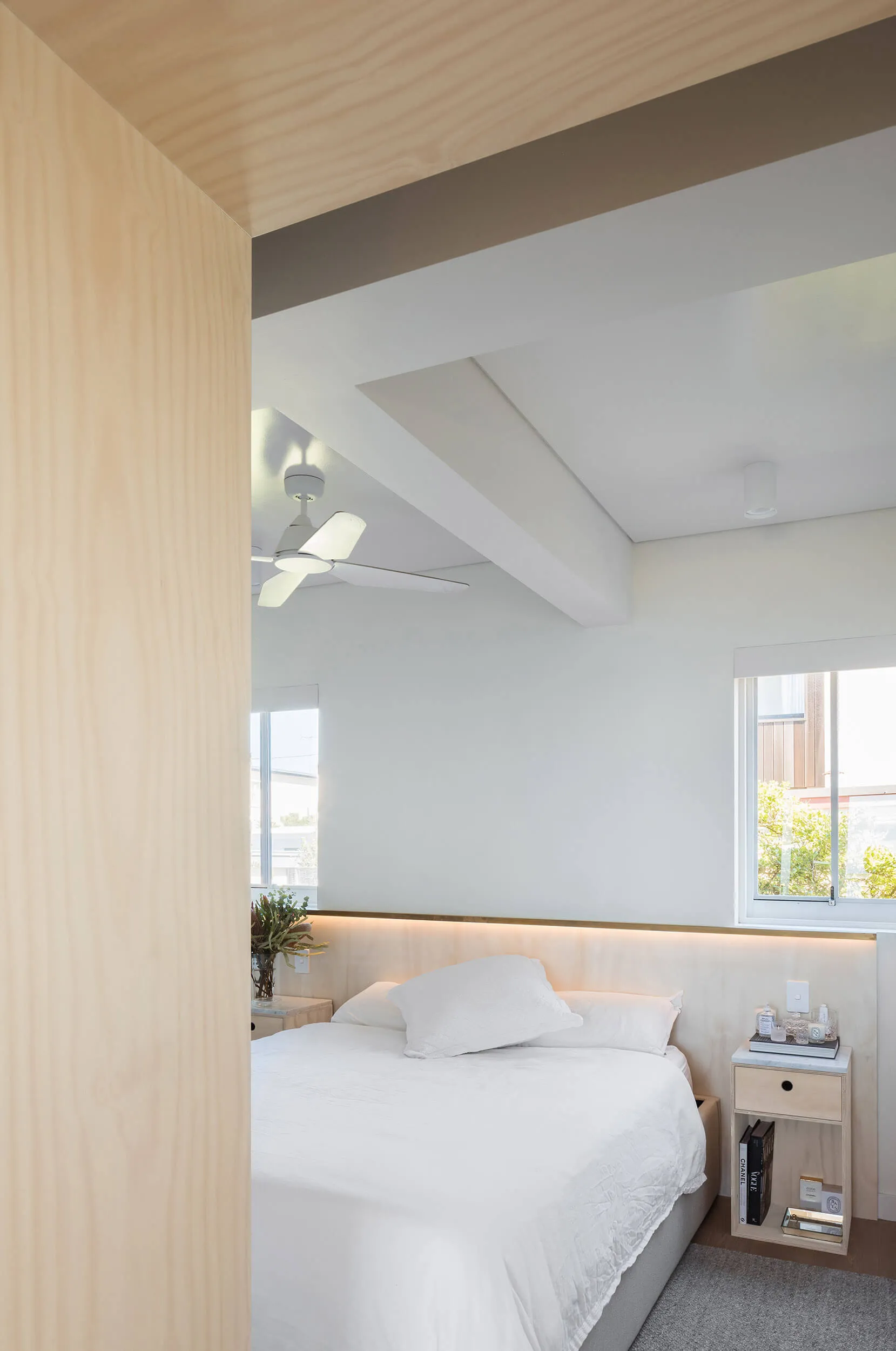 A modern minimalist bedroom featuring a bed with white sheets and a wooden headboard against a white wall, supplemented by am