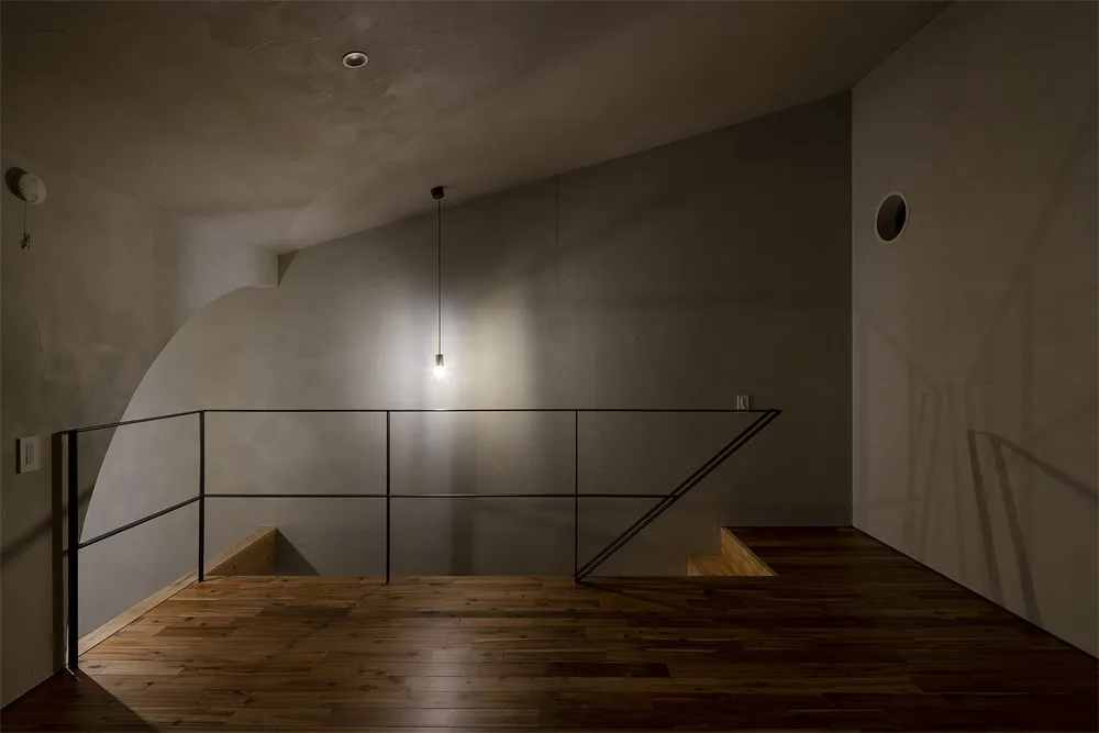 Minimalist staircase with a wooden floor and concrete walls, illuminated by a hanging light fixture.