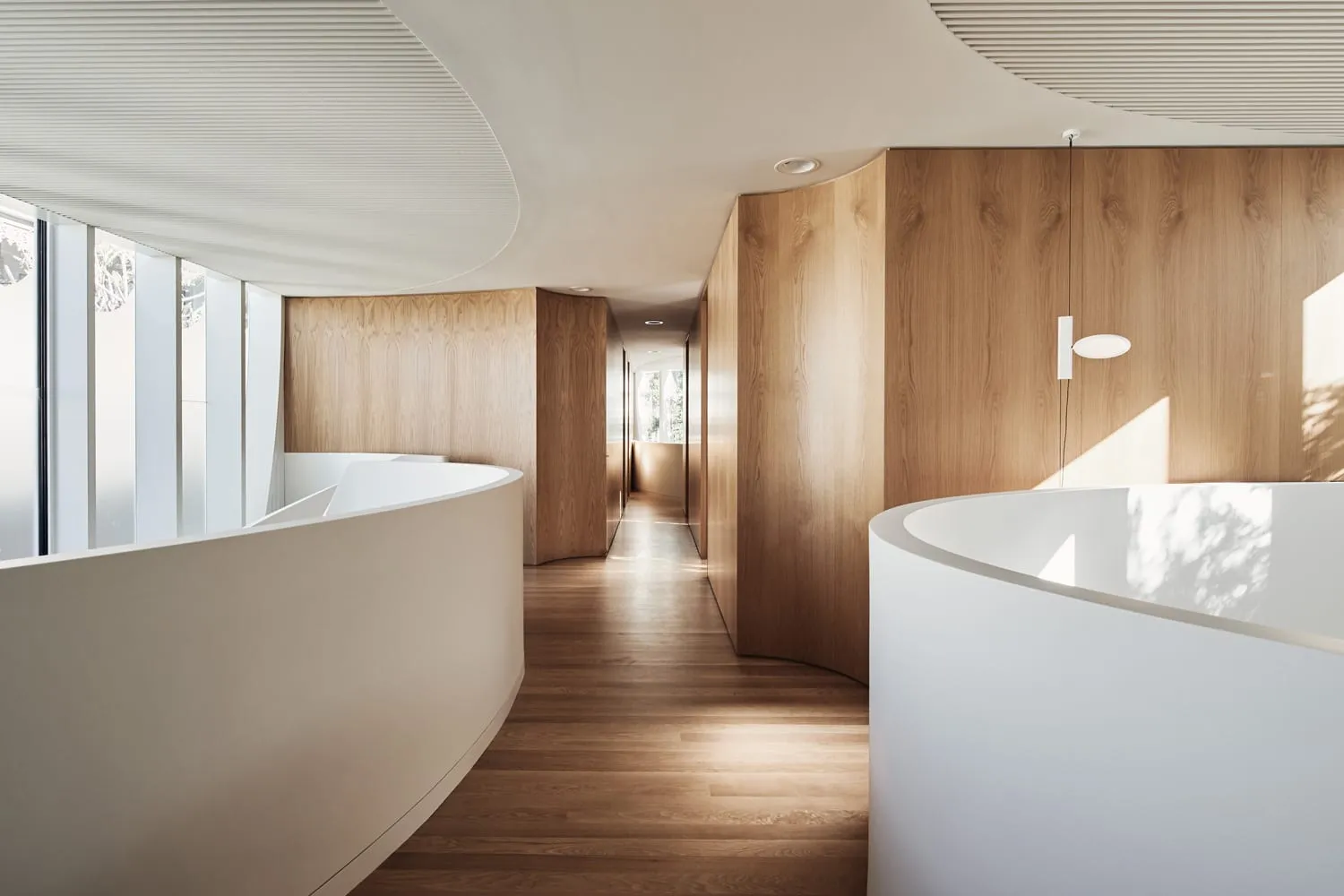 Modern office space featuring curved wooden walls and white reception desks.