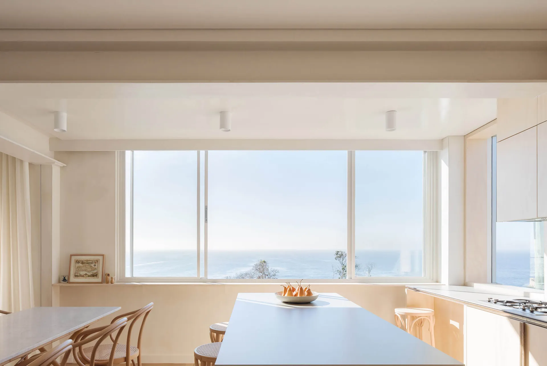 A modern kitchen featuring white materials and a stunning ocean view.