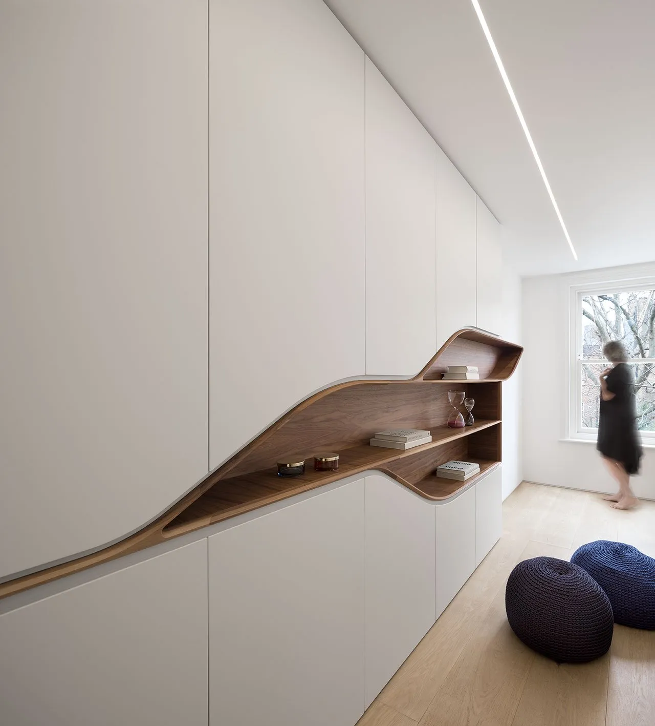 A modern bedroom featuring a sleek, organic-shaped wood shelf integrated into white cabinetry.