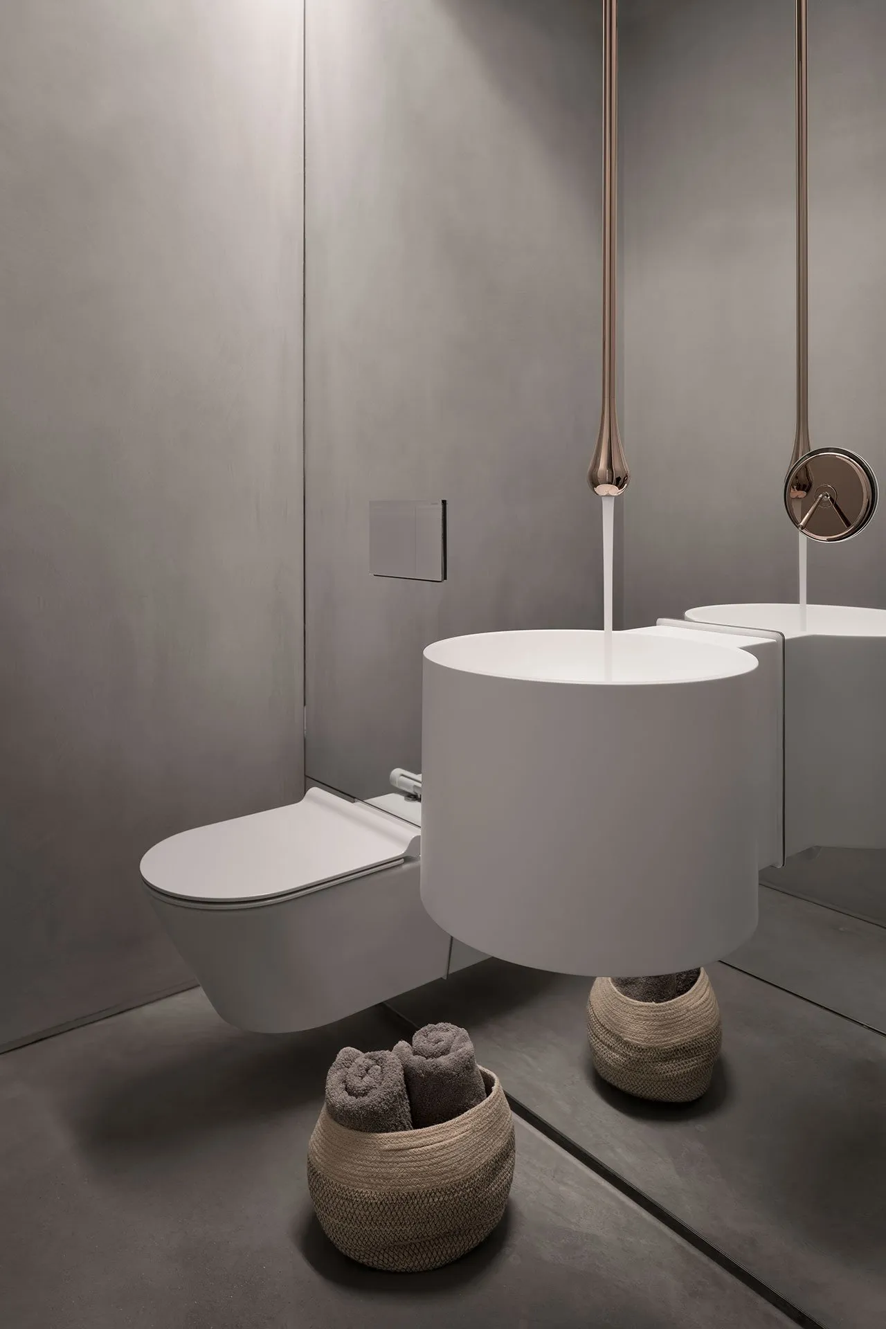 A sleek, modern minimalist bathroom featuring a white ceramic toilet and sink, with a metallic tap and a basket of gray towel