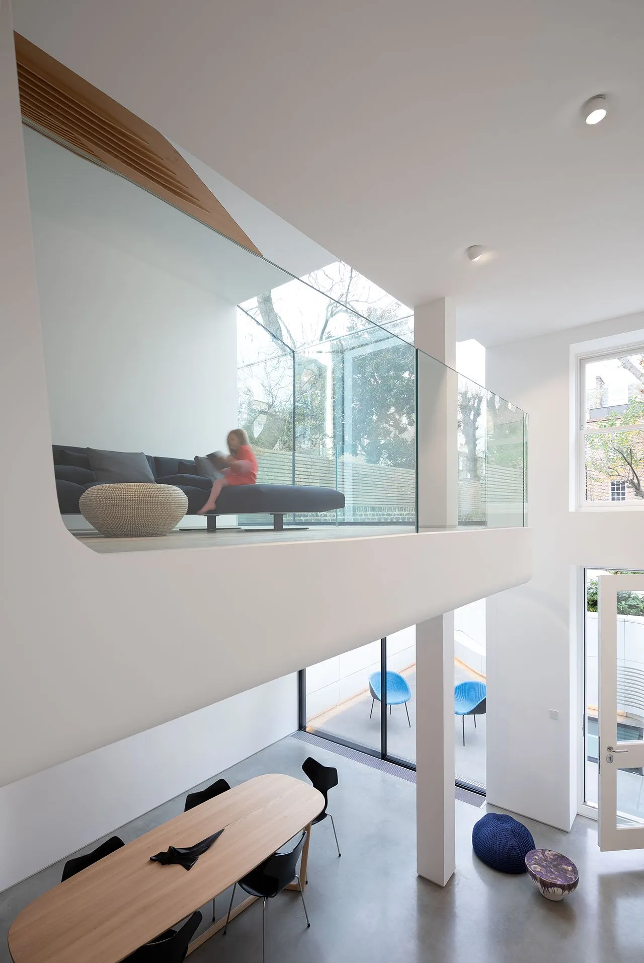 A modern minimalist living room features glass walls, a concrete floor, and a white color palette.