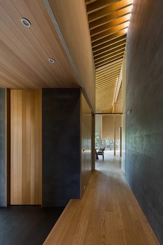 A modern residential corridor featuring wood flooring and concrete walls.