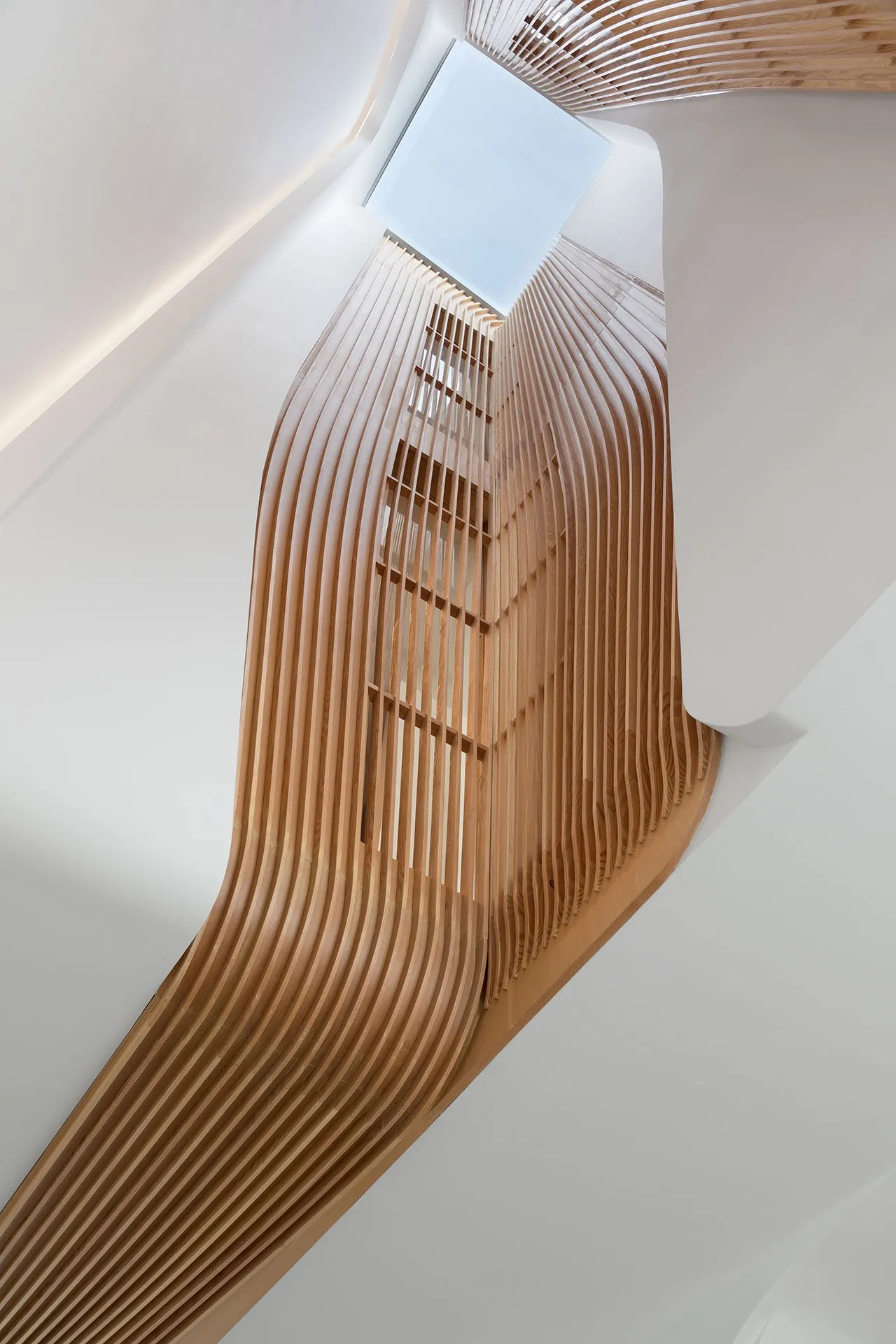 A modern staircase with wooden slats leading up to a skylight.