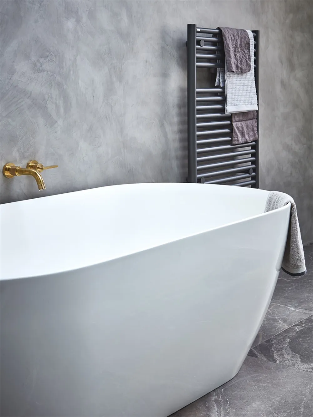 Modern minimalist bathroom featuring a freestanding tub in a freestanding position, with a gray wall and towel rack.