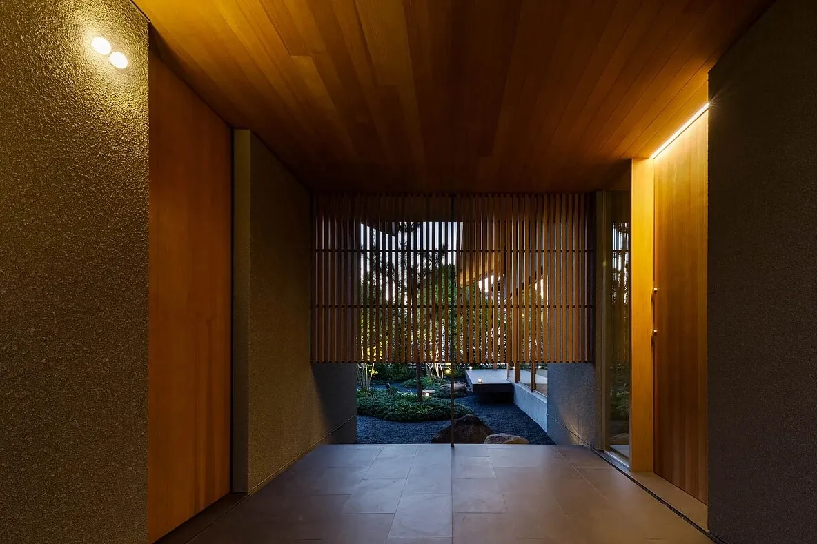 A modern interior space with wooden walls and a stone floor, featuring a view into a serene courtyard.