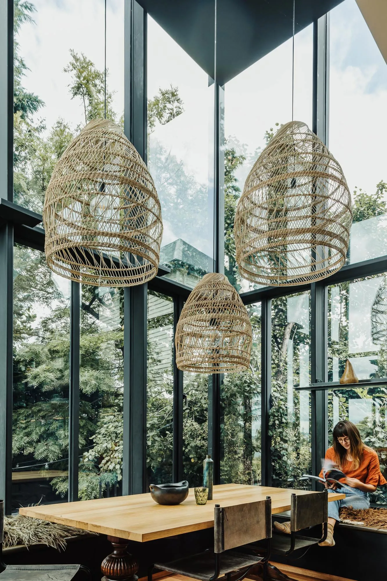 A modern living room with cane pendant lights and a large glass window overlooking greenery.