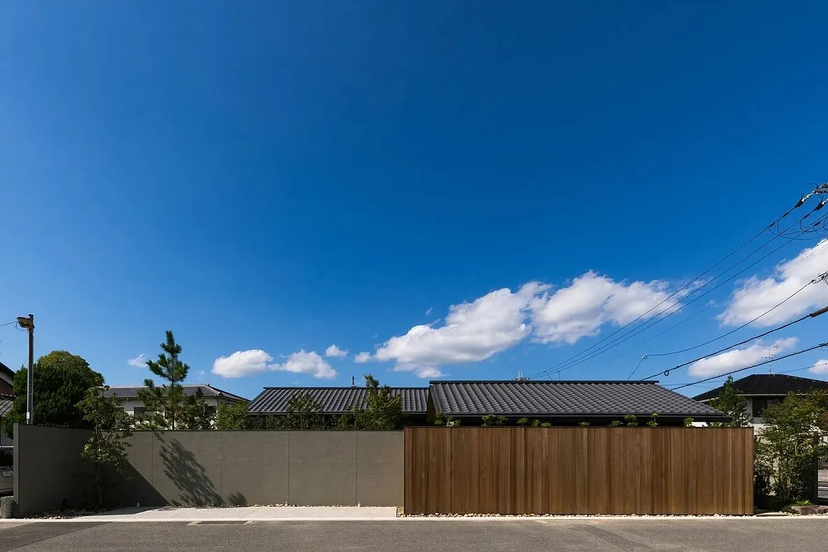 Modern residential house with metal roof and wooden fence against a clear blue sky.