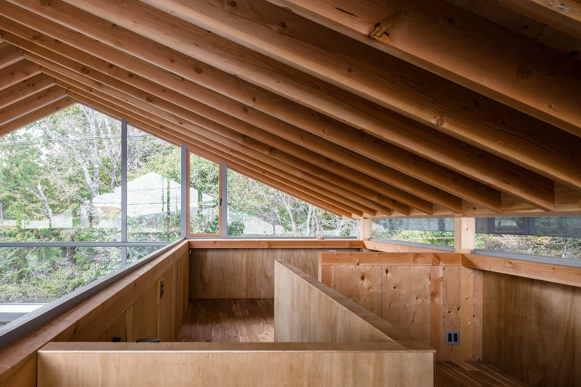 A modern attic space with a wooden ceiling, exposed beams, and large windows showcasing a forest view.