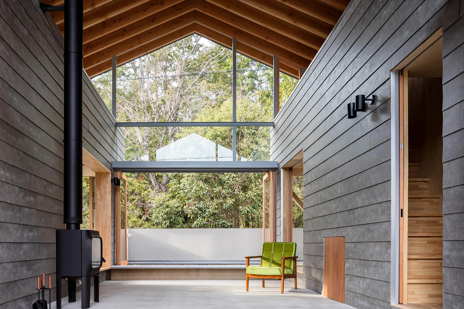 A modern, minimalist interior with concrete walls, large windows, and a green armchair.