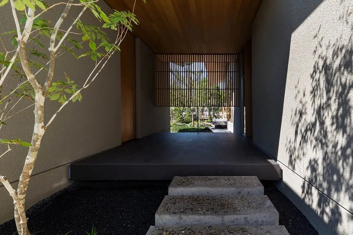 Concrete entrance with wood slat screen and plants, leading to a garden.