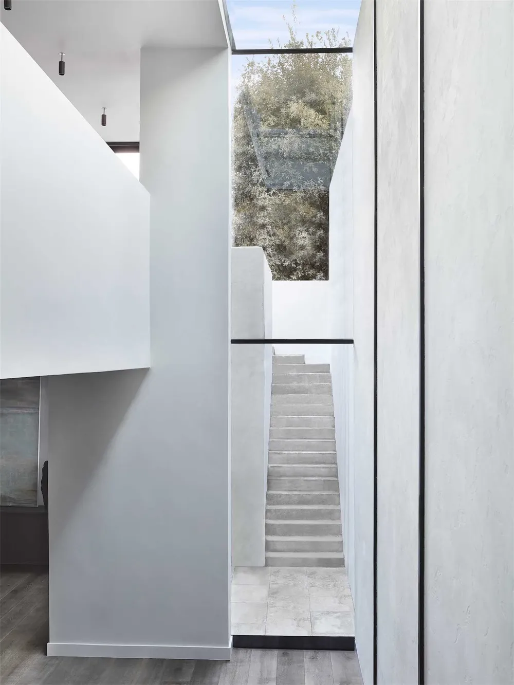 Modern minimalist concrete staircase leading through a white minimalist hallway.