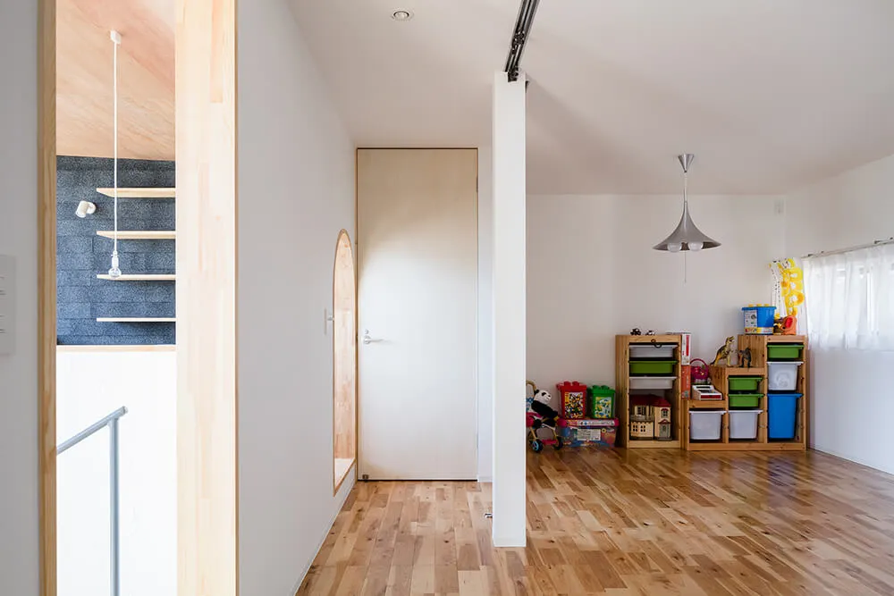 A modern playroom with natural wood flooring and shelves, featuring colorful toys on a wooden floor.
