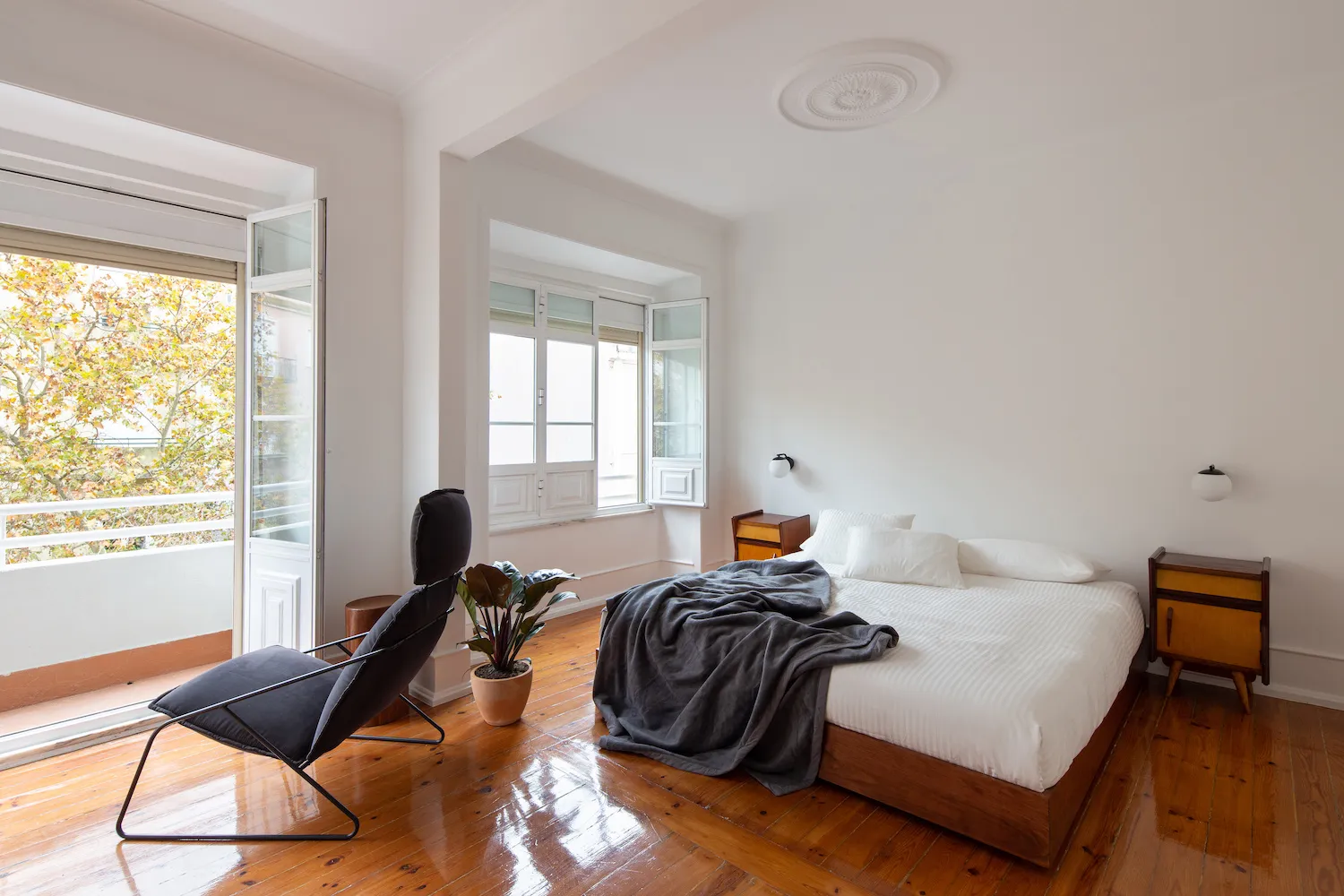 簡約臥室搭配木地板,床上鋪著灰色毯子,並擺放一張現代黑色椅子。