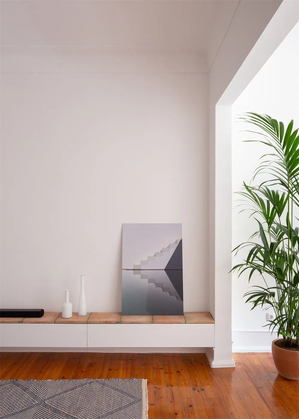 A minimalist living space featuring concrete surfaces, wooden furnishings, and potted green plants.