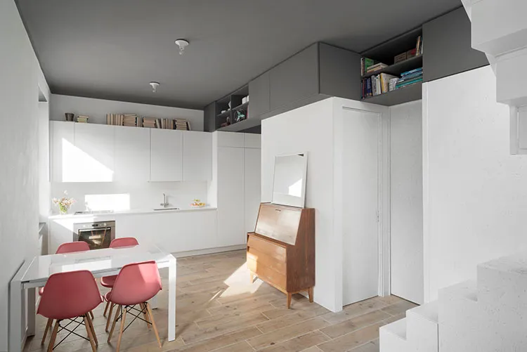 A minimalist modern kitchen with white cabinets, a glass dining table, and pink chairs.