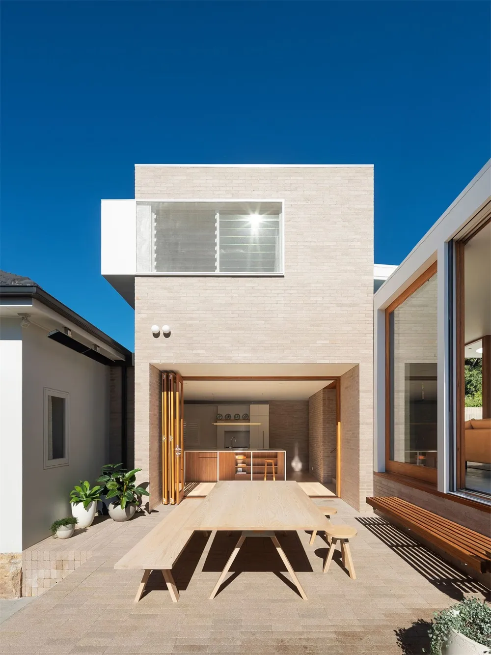 Modern residential exterior with brick façade, large glass windows, and outdoor seating area.