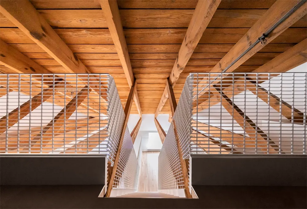 A minimalist staircase featuring wooden beams and metal railings viewed from above.
