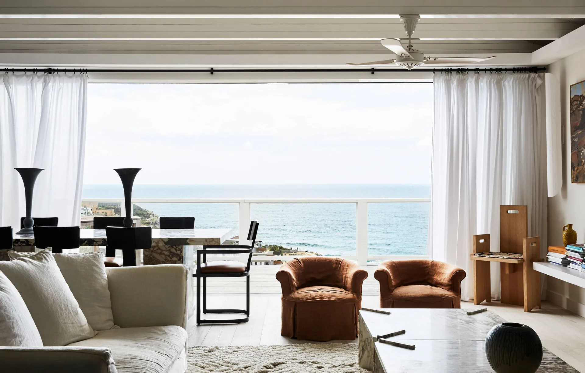 A minimalist living room with a large window overlooking the ocean, featuring fabric seating and modern furniture.