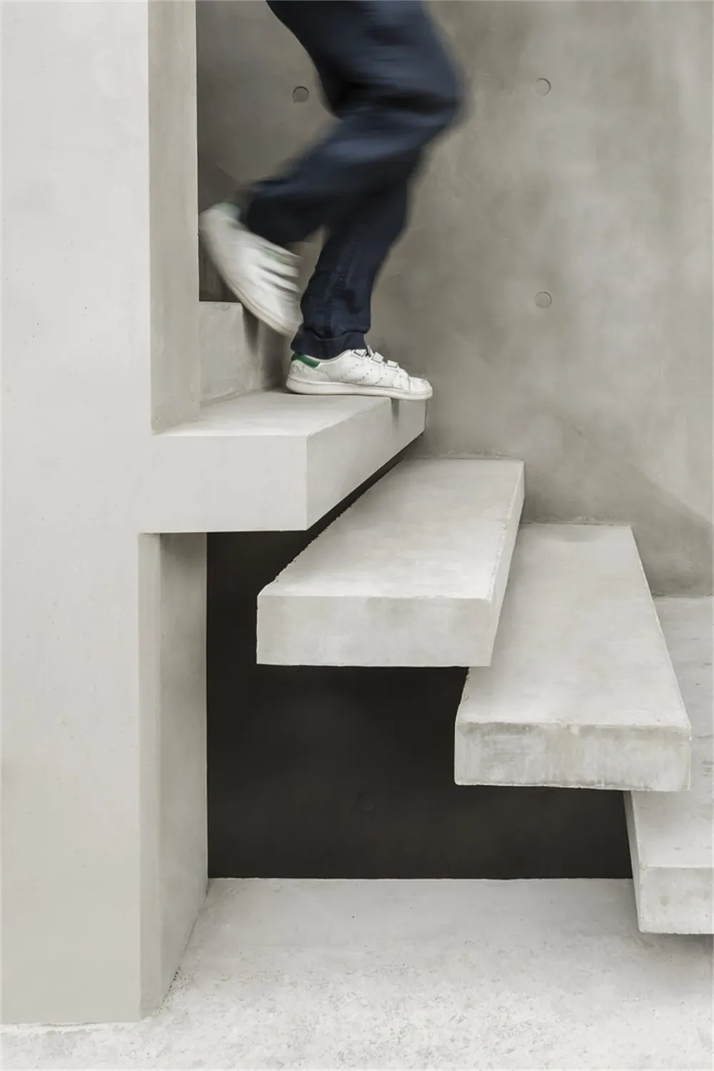 A modern staircase constructed from white concrete with a person wearing white sneakers with green straps climbing it.