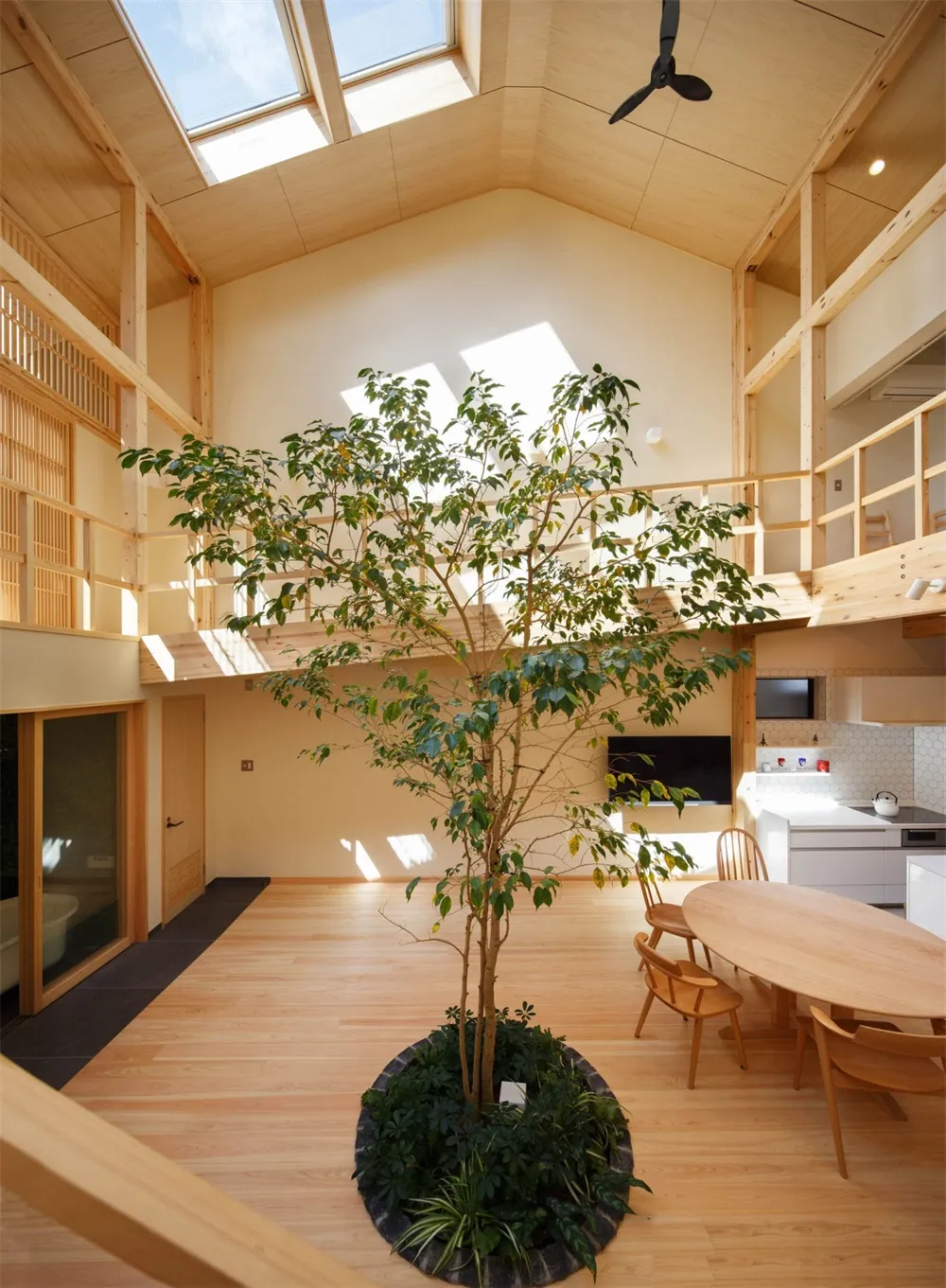 A minimalistic residential interior space with wooden flooring, a central tree, and open-concept design.