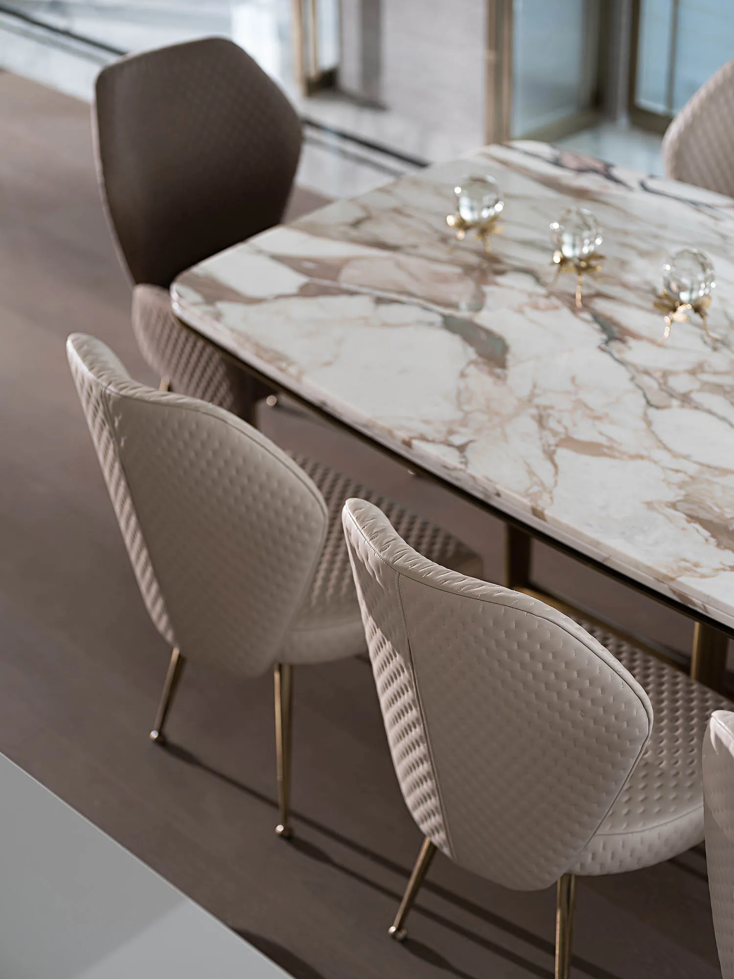 Modern dining room with white and brown marble table and leather upholstered chairs with brass legs.