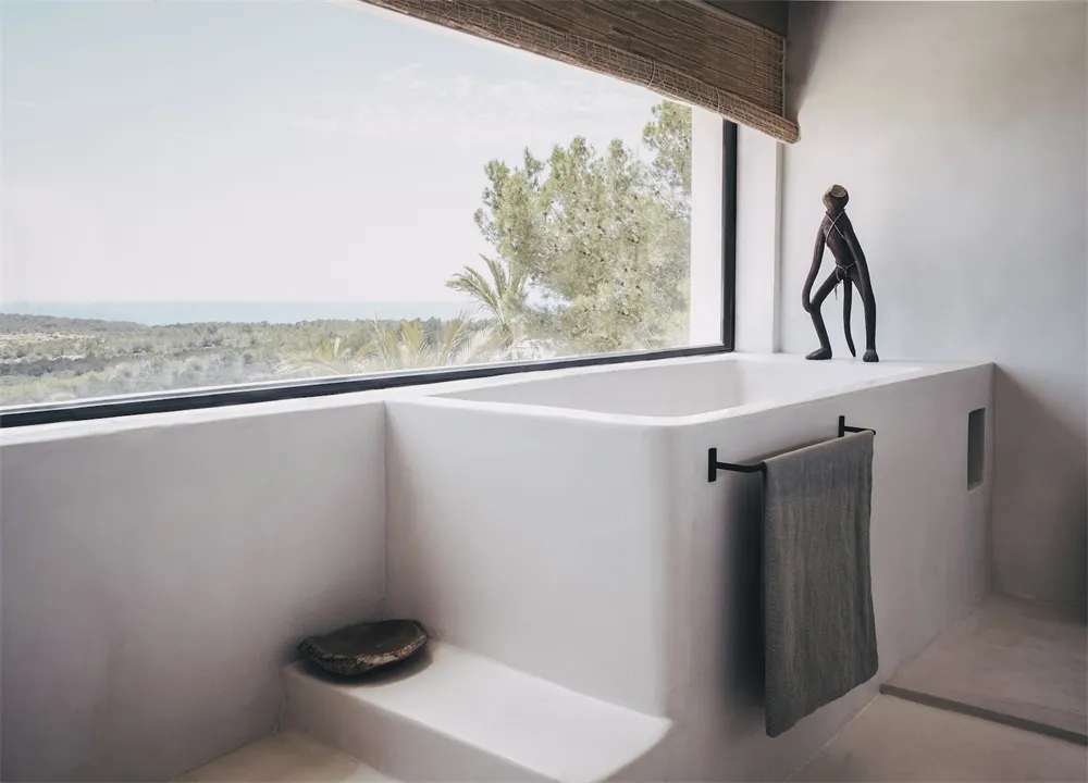 Modern minimalist bathroom featuring a concrete bathtub and towel rack with a view of the ocean through a large window.
