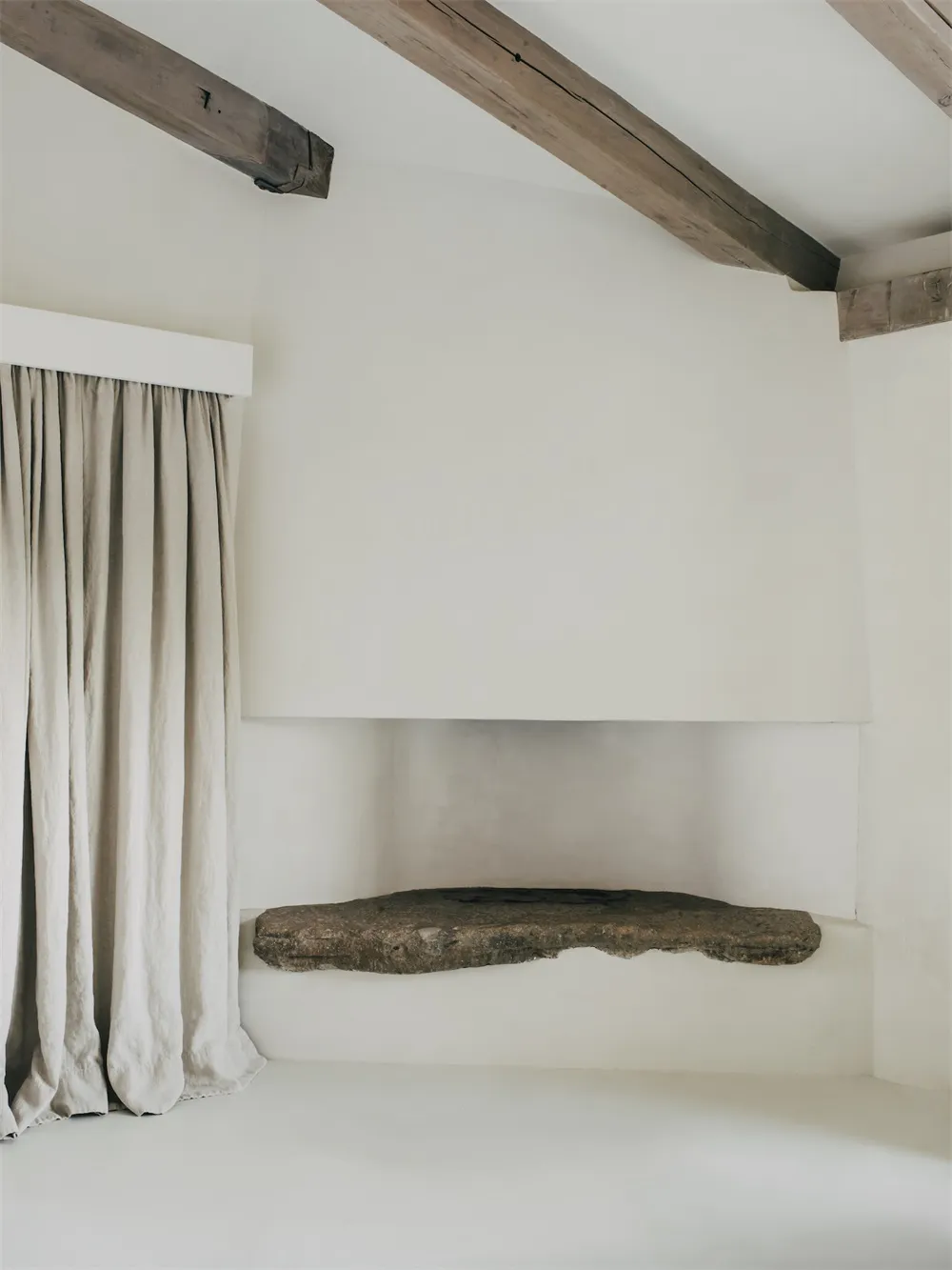 A minimalist interior featuring a corner stone fireplace with a concrete finish.