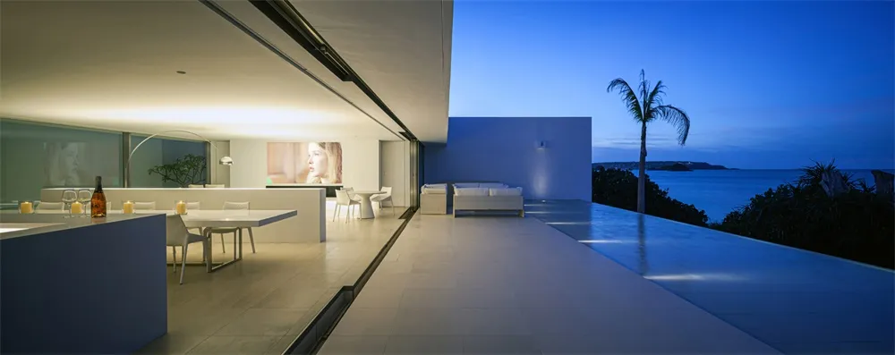 Modern minimalist residential interior with glass walls overlooking the ocean at dusk