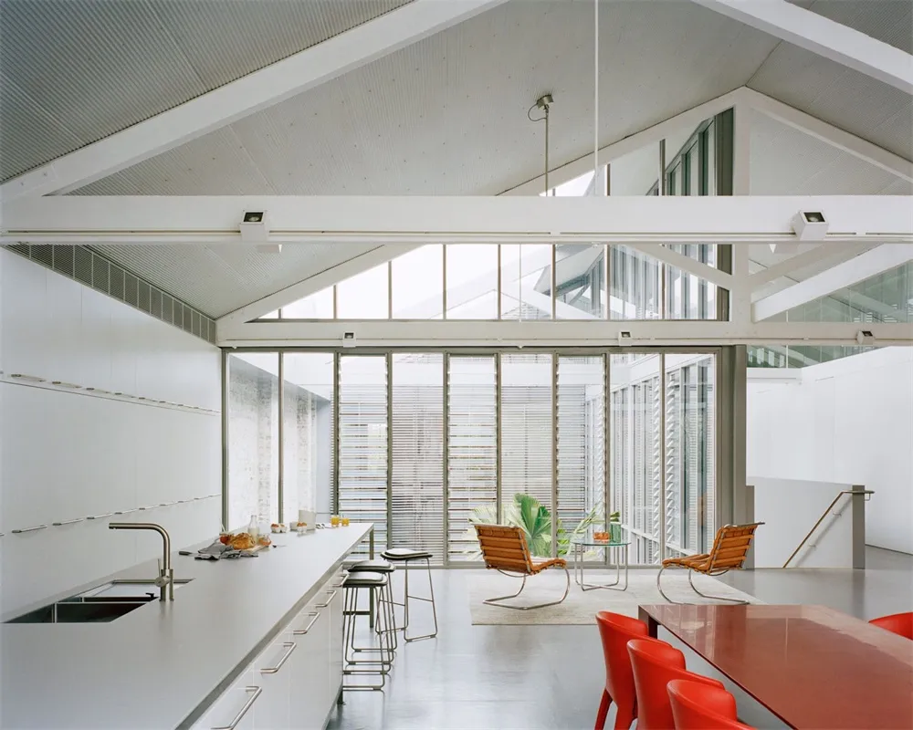 Modern minimalist kitchen with metal cabinets, glass walls, and red wooden tables